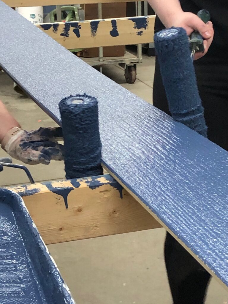 Two paint rollers on painting blue on a piece of siding.