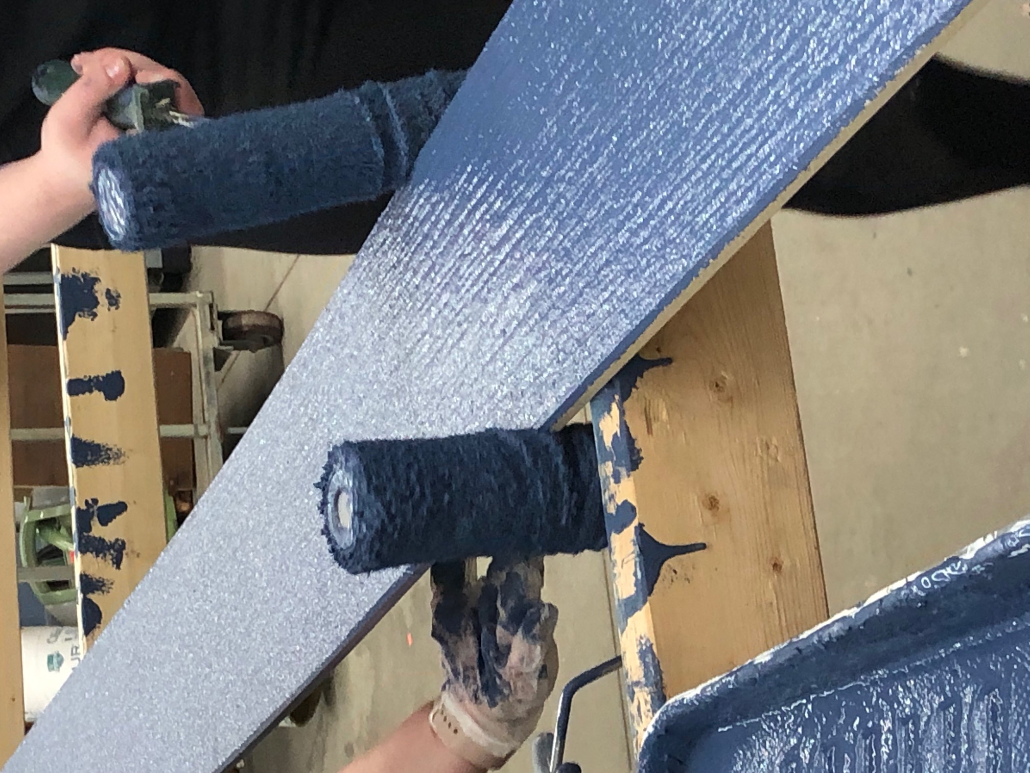 Two paint rollers on painting blue on a piece of siding.